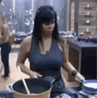 a woman is cooking in a kitchen while holding a pan and a spoon .