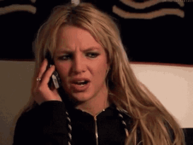 a blonde woman is talking on a cell phone and making a funny face .