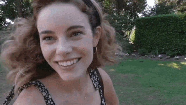 a woman wearing a headband and earrings smiles in a park