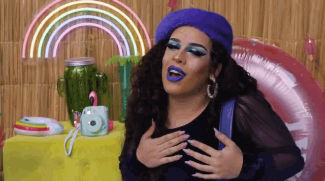 a woman with blue makeup and a purple beret holds her hands over her chest