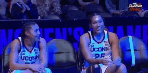 two uconn women 's basketball players are sitting next to each other in the stands during a game .