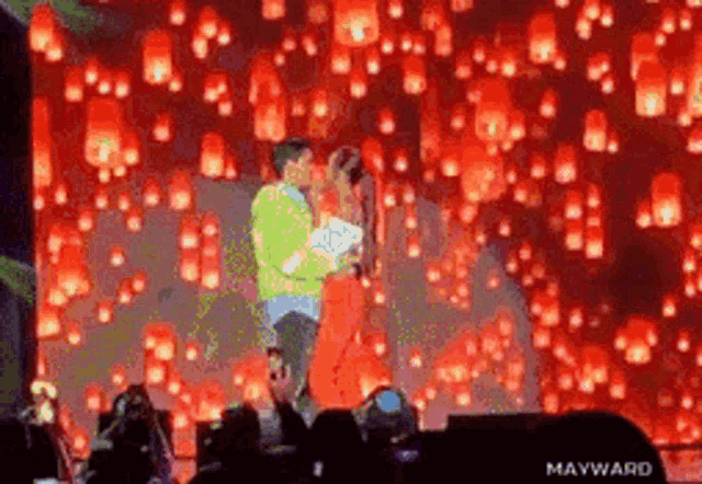 a man and a woman are kissing on a stage with lanterns falling from the sky behind them