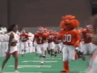 a group of football players are running on a field with a mascot wearing a jersey with the number 10 on it