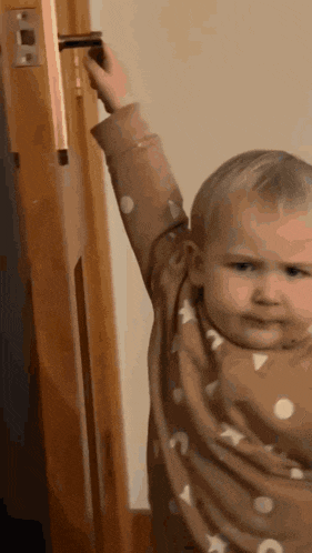 a baby is reaching for a door handle and making a face .