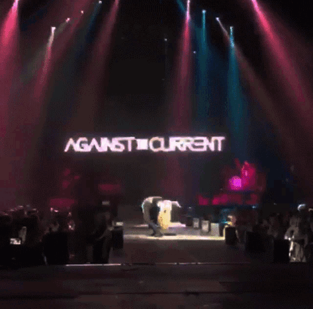 a woman playing a guitar on a stage with against current written on the screen