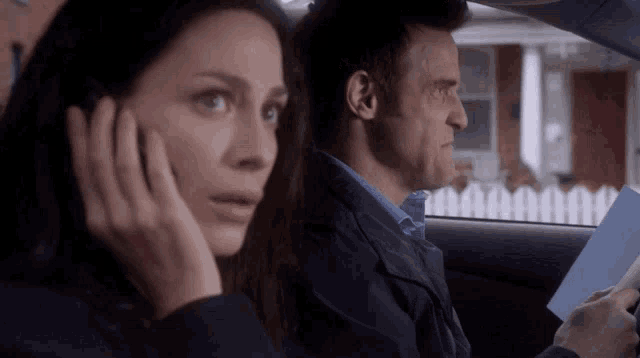 a man and a woman are sitting in a car and the woman is talking on a cell phone