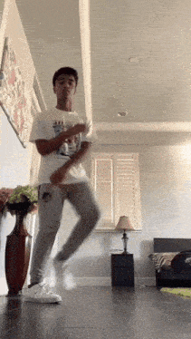 a young man is dancing in a living room wearing a t-shirt that says ' a ' on it