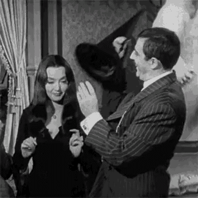 a man and a woman are standing next to each other in a room . the woman is wearing a black dress .