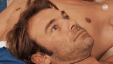 a shirtless man with a beard is laying on top of another shirtless man on a bed .