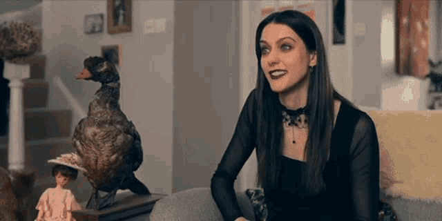 a woman sits on a couch next to a stuffed duck