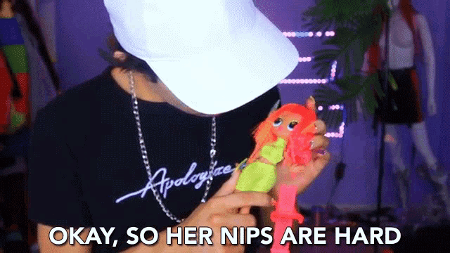 a man in a white hat is holding a doll and says okay so her nips are hard on the bottom