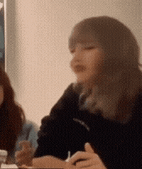 a woman is sitting at a table with a pen in her hand and making a face .