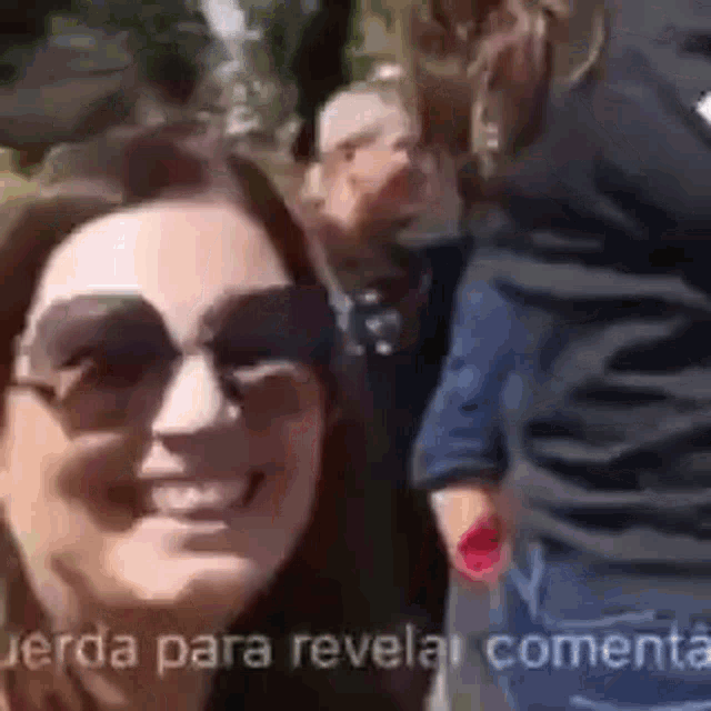 a woman wearing sunglasses is taking a selfie with a man in the background .