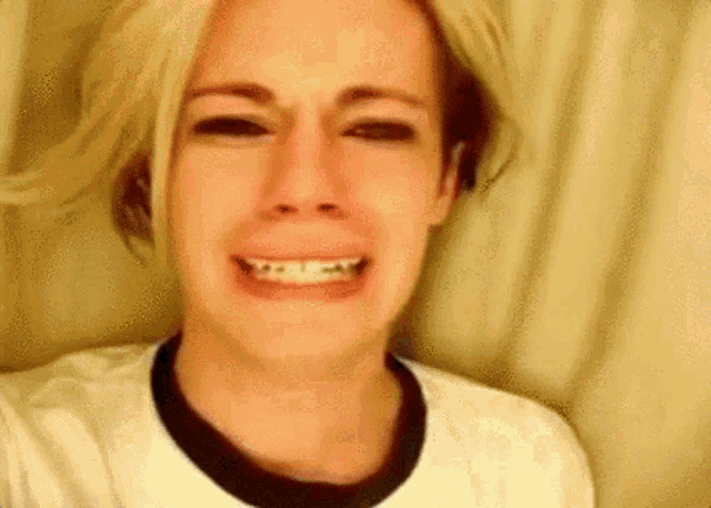 a woman with blonde hair is crying and smiling while wearing a white shirt