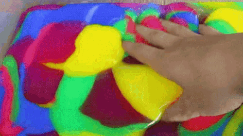 a person 's hand is playing with a rainbow colored slime .