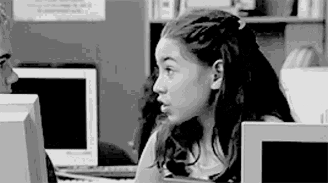 a black and white photo of a girl sitting in front of a computer monitor .