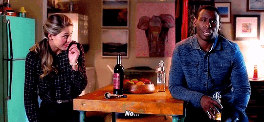 a man and a woman are sitting at a table with a bottle of wine on it and the word no on the table