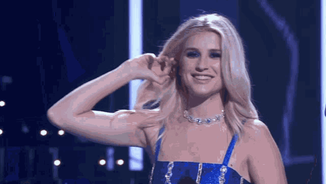 a woman in a blue dress is smiling and covering her ears with her hand