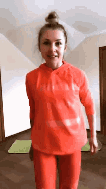 a woman in a red hoodie and red pants is standing on a yoga mat .