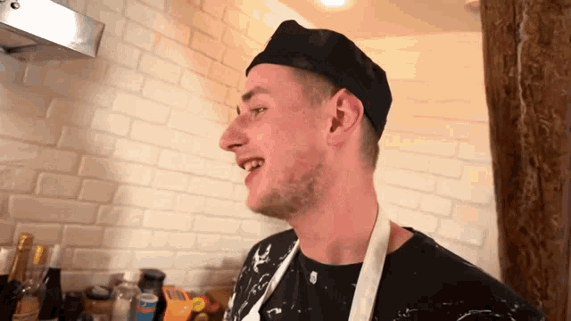 a man wearing a chef 's hat and apron stands in front of a white brick wall
