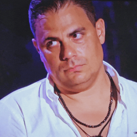 a close up of a man wearing a necklace and a white shirt with the letter t on the collar