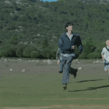 a group of people are running in a field with mountains in the background .