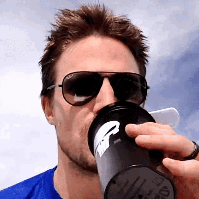 a man wearing sunglasses and a blue shirt is drinking from a black cup