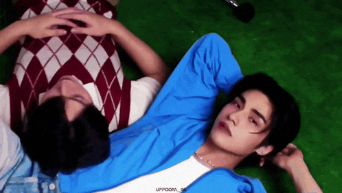 two young men are laying on a green carpet and one of them has the word uppoom on his shirt