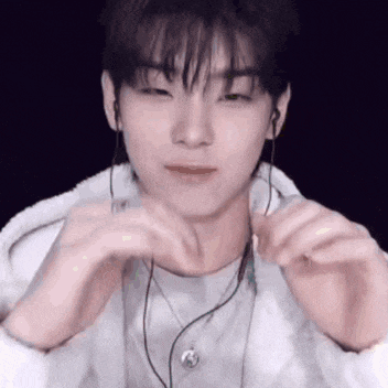 a young man wearing earphones and a necklace is making a heart shape with his hands .