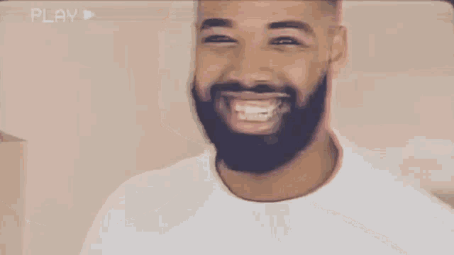 a man with a beard is smiling and wearing a white t-shirt .