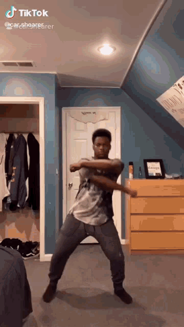 a young man is dancing in a room with a blue wall and a yellow dresser .