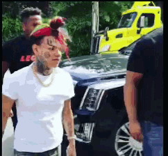 a man with a tattoo on his face stands in front of a car