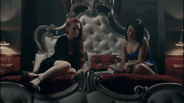 a couple of women sitting on a bed talking to each other