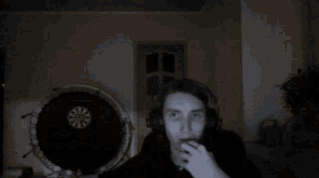 a man is wearing headphones and smoking a cigarette in front of a dart board .