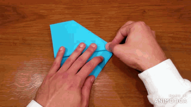 a person is folding a piece of blue paper and the words made in animatica are visible