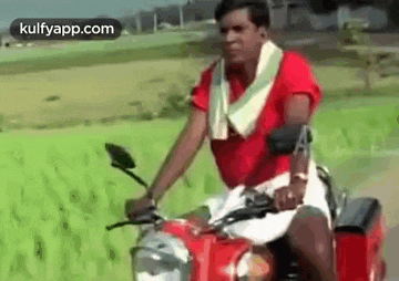a man in a red shirt and white shorts is riding a red motorcycle on a road .
