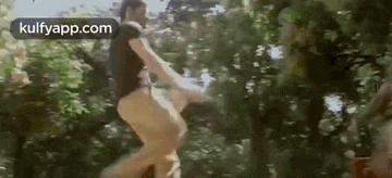 a man is jumping in the air in a forest while holding another man 's leg .
