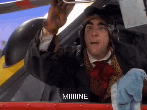 a man wearing a helmet and gloves says " miiiiiine " in front of a plane