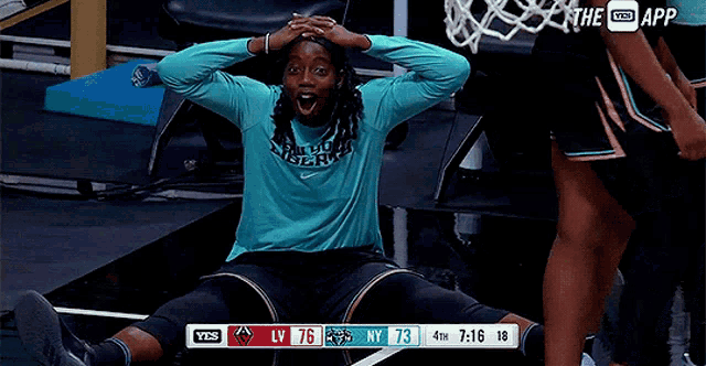 a basketball player is sitting on the floor with his hands on his head in front of a scoreboard that says the app