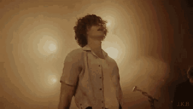 a man with curly hair is standing in front of a microphone on stage .