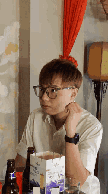a man wearing glasses sits at a table with a box of fuji chips