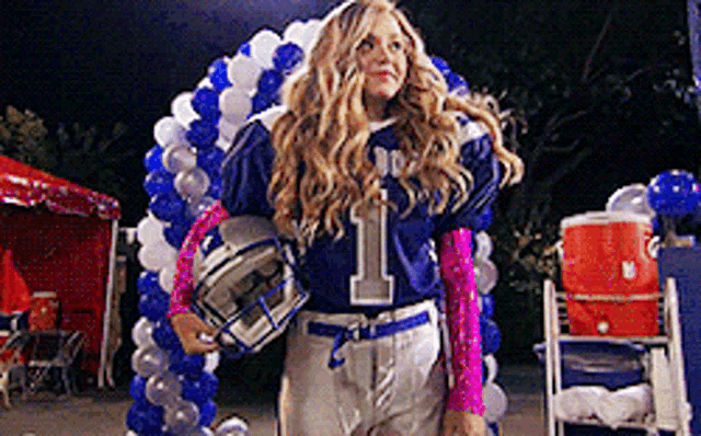 a woman in a football uniform is holding a helmet in front of balloons