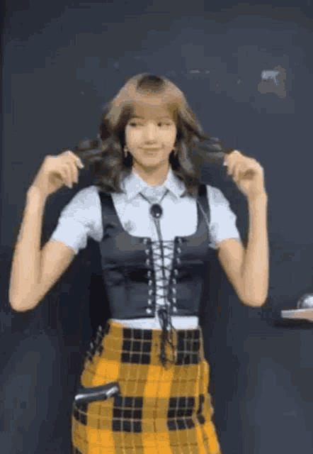 a woman wearing a plaid skirt and a black vest is standing in front of a black wall .