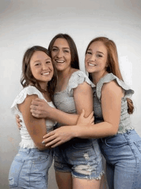 three young women are hugging each other and smiling while posing for a picture .