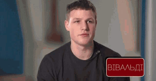 a young man in a black shirt is sitting in front of a sign that says ' вивалдi ' on it