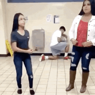 two women are standing next to each other on a tiled floor while a man kneels on the floor .