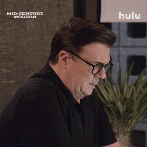 a man wearing glasses is sitting in front of a screen that says hulu