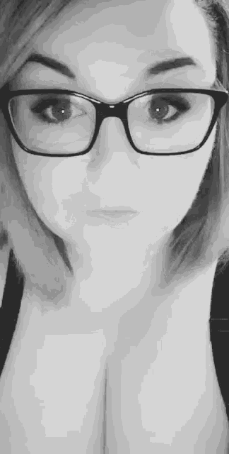 a black and white photo of a woman wearing glasses and a bra .