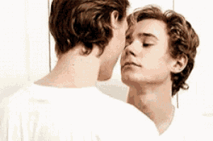 a man is kissing another man on the forehead in front of a mirror .
