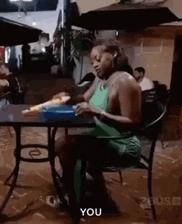 a woman in a green dress is sitting at a table with a box of food .